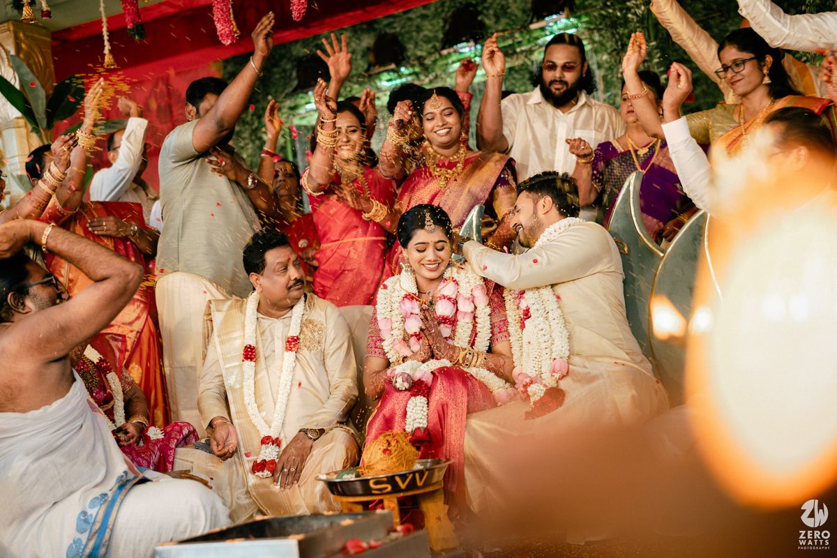 Vibrant Indian wedding ceremony with bride and groom exchanging garlands surrounded by joyful guests celebrating.