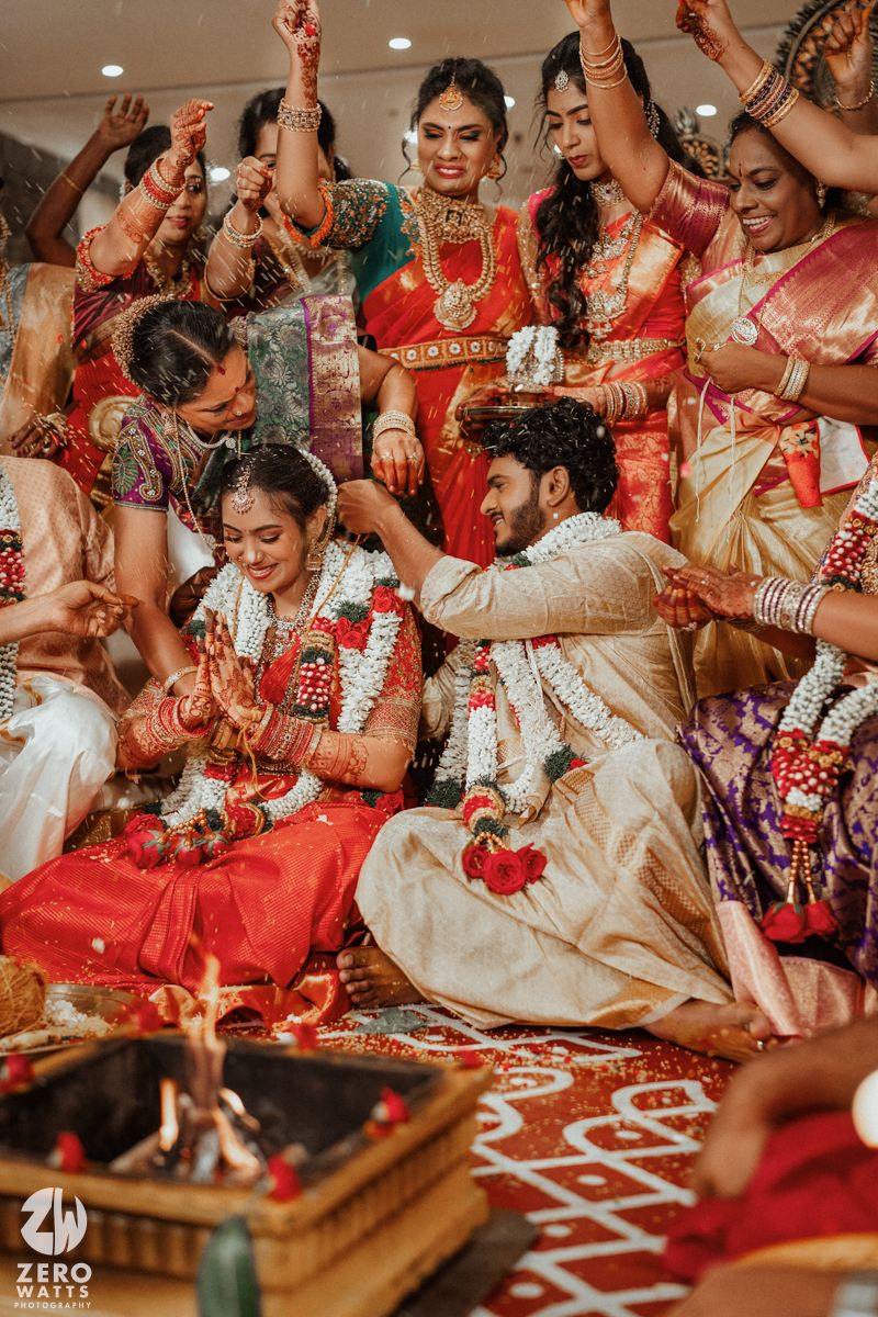 Joyful South Indian wedding ceremony with bride in red saree and groom surrounded by celebrating family members.