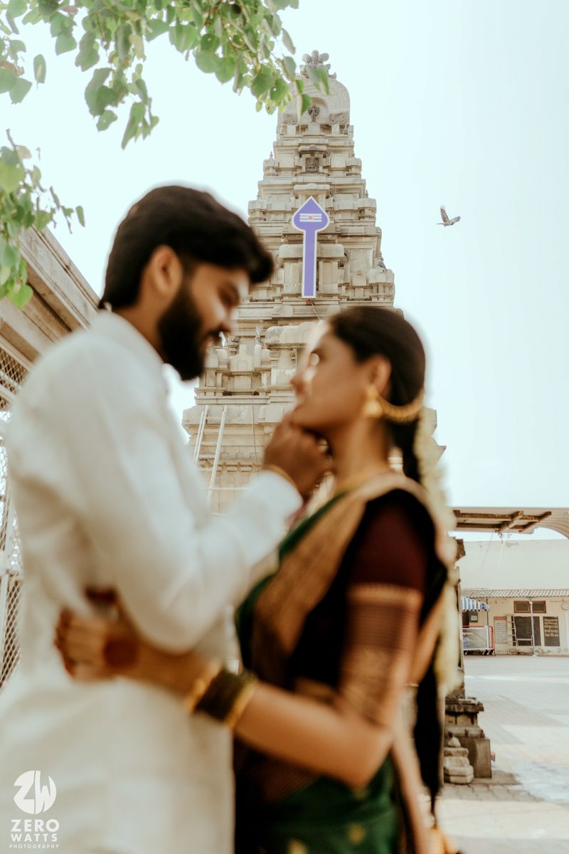 Couple in traditional South Indian attire posing near a temple gopuram, bride in green saree with gold jewelry.