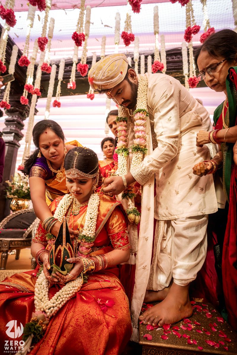 Groom places mangalsutra on bride during traditional South Indian wedding ritual surrounded by family members.