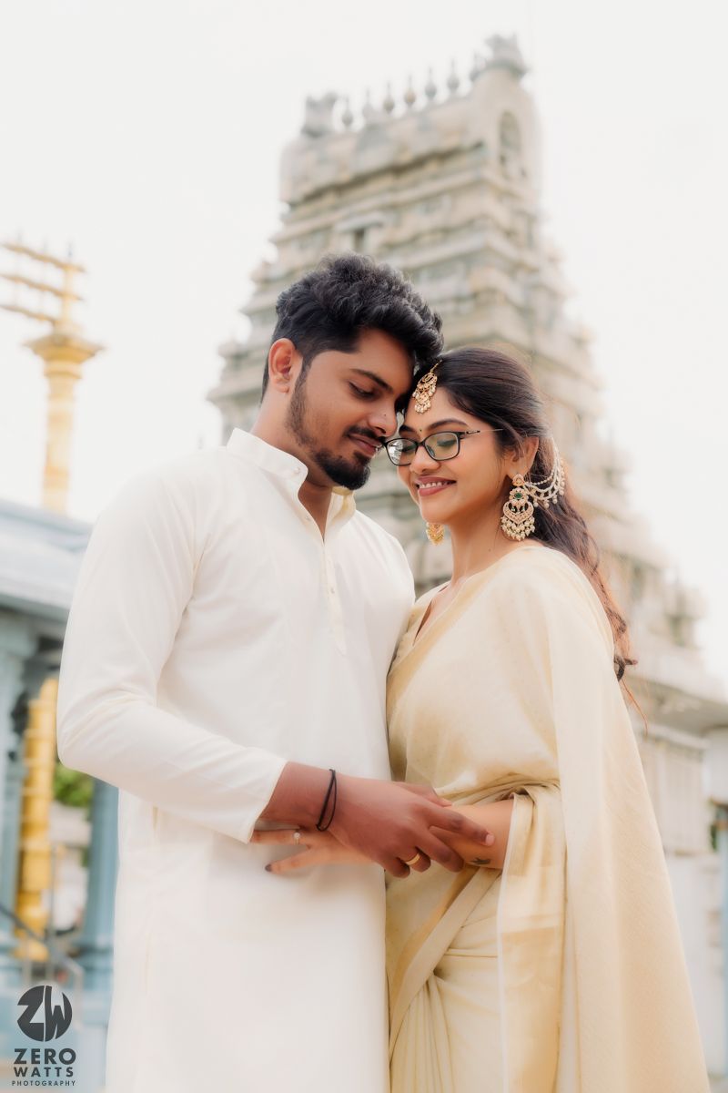 Couple in traditional white attire share romantic moments near temple spires.