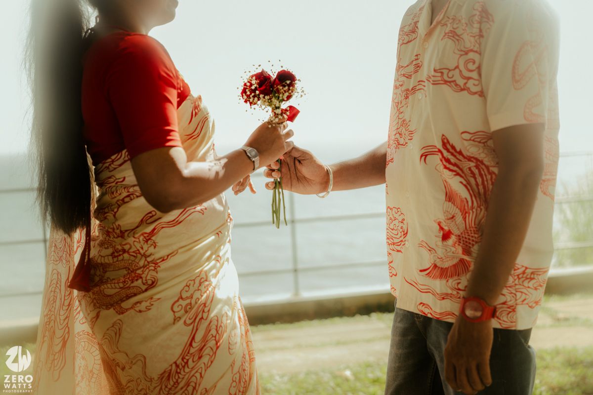 A couple in coordinated red and white outfits embrace in a romantic outdoor setting during golden hour.
