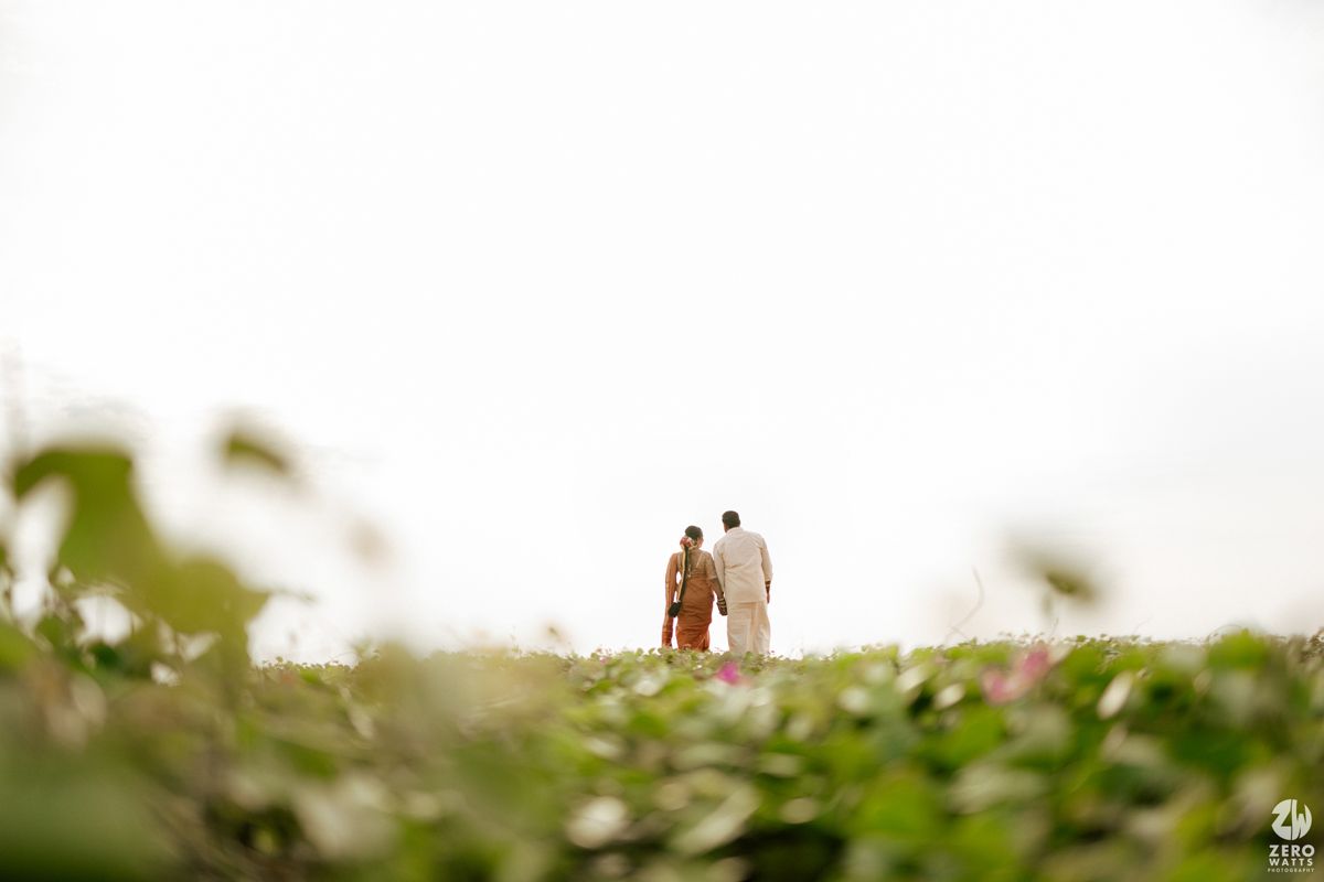 A couple walks through a lush green field of blooming flowers on a sunny day.