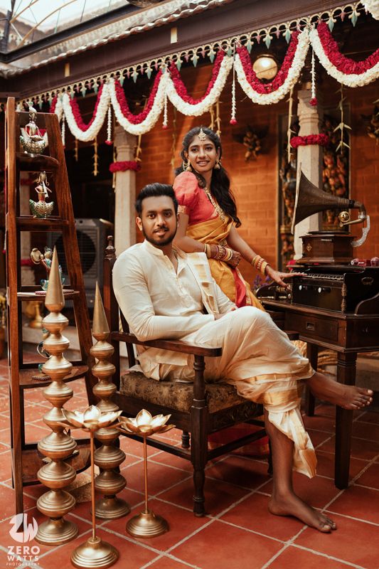 South Indian couple in traditional attire posing with brass diyas and floral garlands during their wedding ceremony.