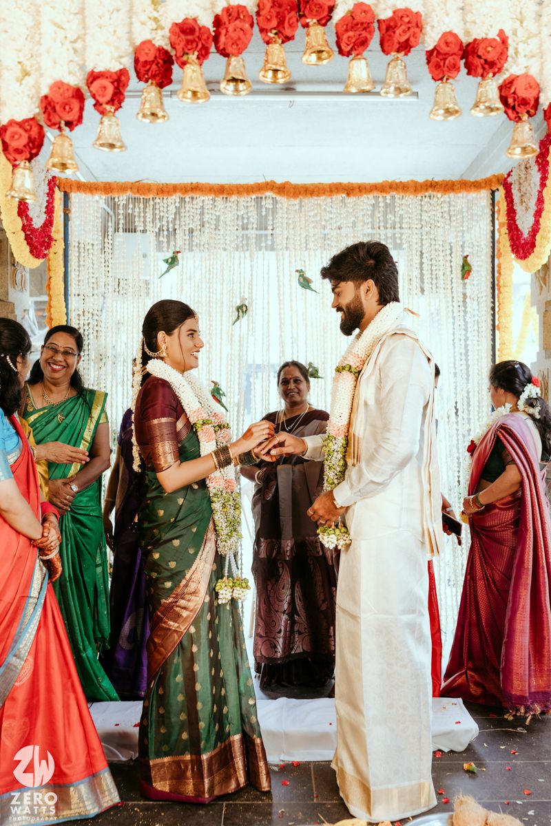 South Indian wedding ceremony with bride in green Kanjivaram saree exchanging garlands with groom under floral mandap.