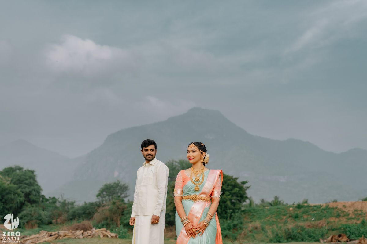 Indian couple in traditional wedding attire posing before misty mountain backdrop.