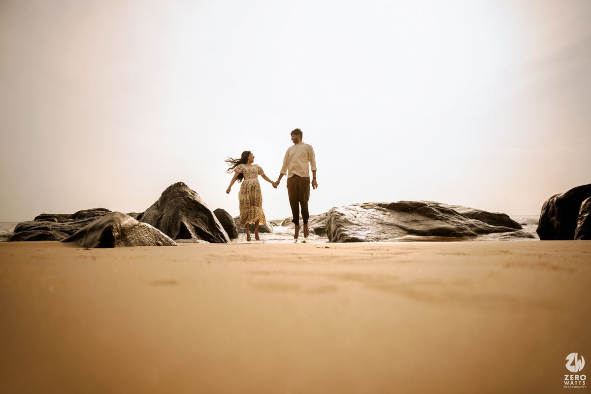 Two silhouettes walk hand in hand across a misty desert landscape at sunset.