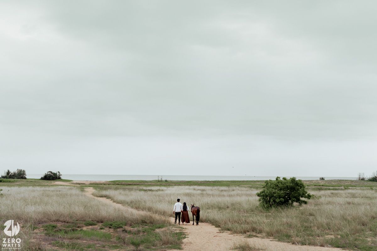 Panoramic view of a vast grassy field with horses and riders in the distance under an overcast sky.