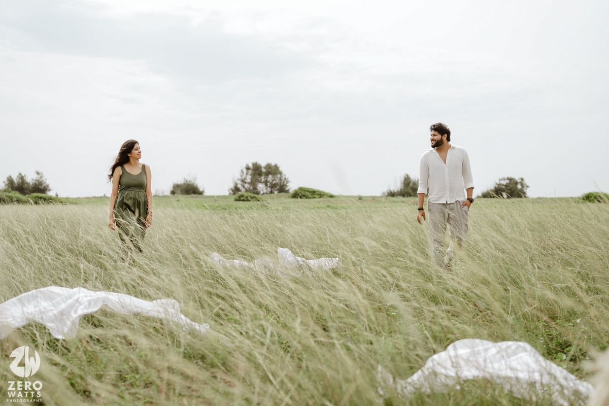 Dreamy outdoor portrait session in golden meadow with couple walking through tall grass and flowing dress.