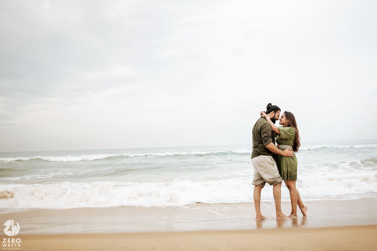 Two people embrace on a misty beach with gentle waves rolling in behind them.