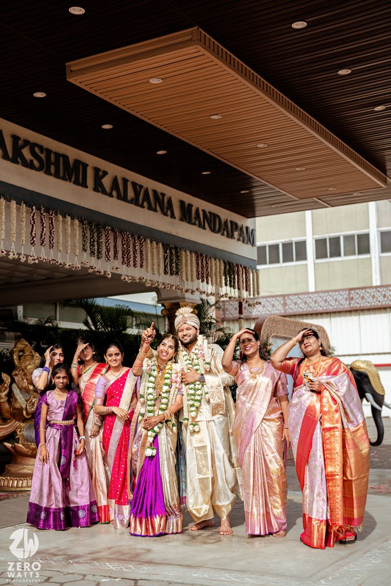 A group wearing colorful traditional Indian wedding attire poses together in a line at an indoor venue.