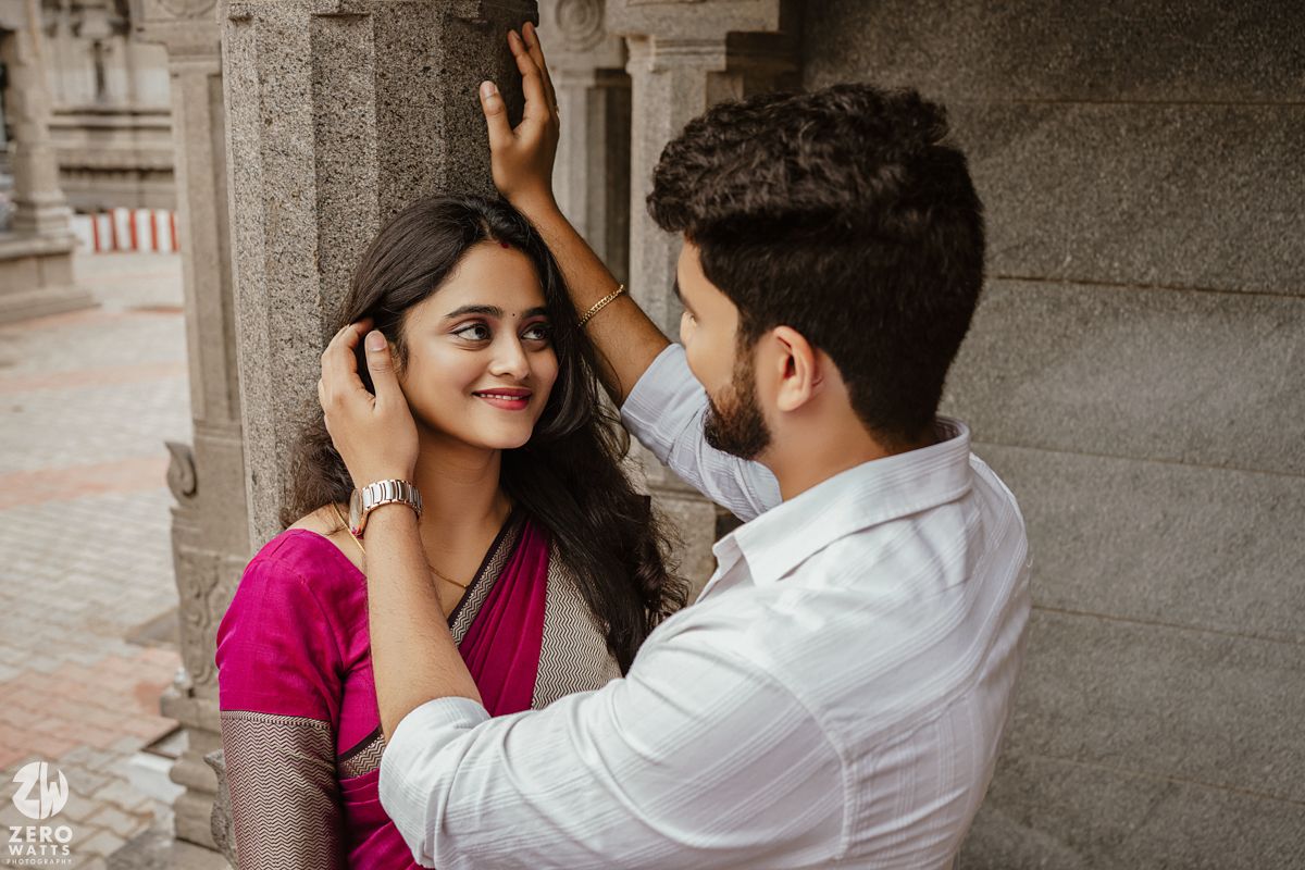 A couple shares a romantic moment in front of a stone architectural backdrop.