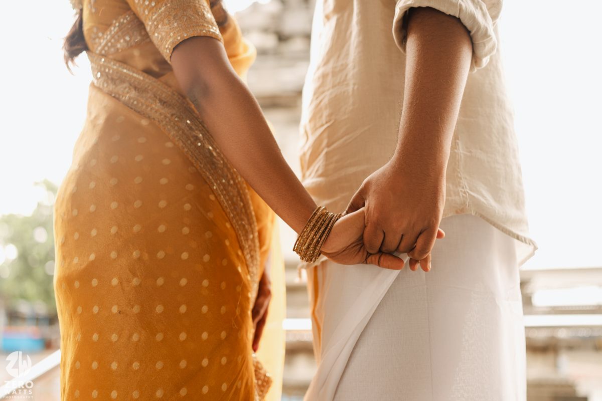 Two people hold hands tenderly while wearing flowy summer dresses in warm sunlight.