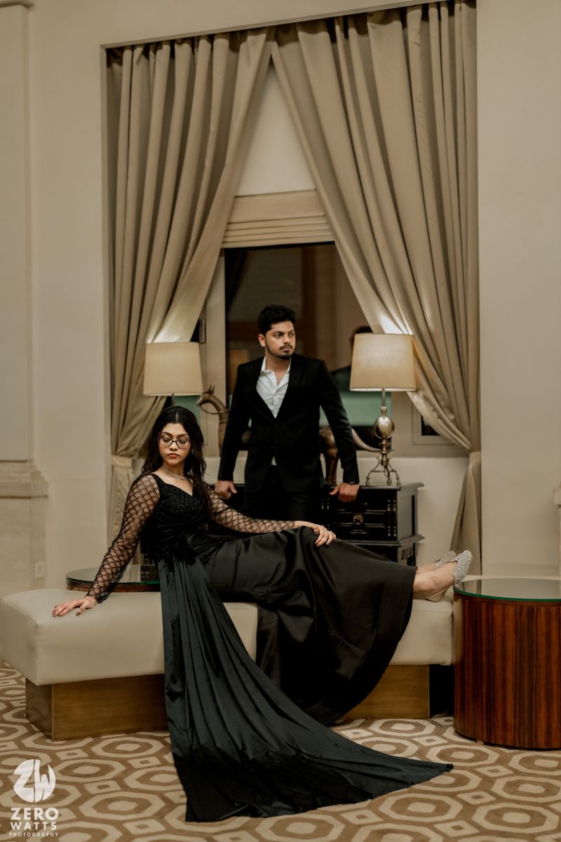 Couple in black formal wear poses dramatically on patterned floor with cream curtains.