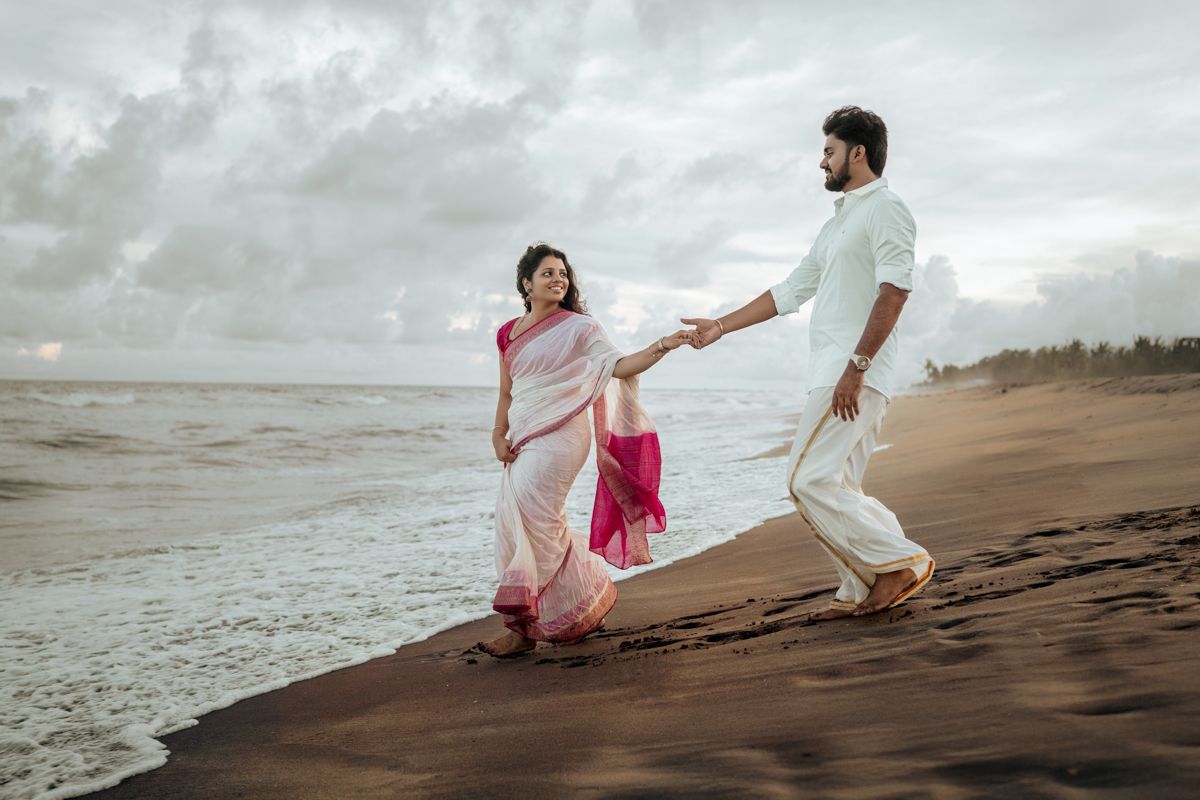 Two people in white outfits walk along a misty beach shoreline at sunset creating a romantic silhouette.