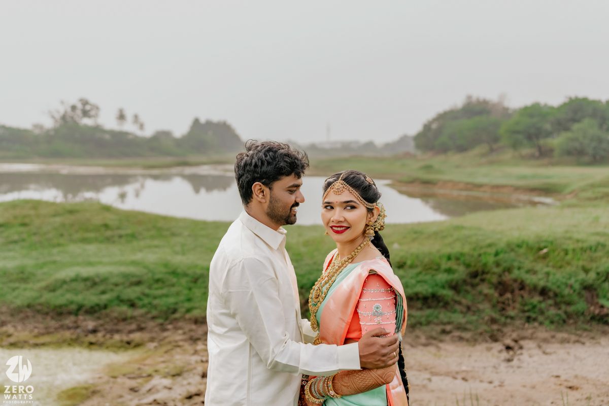 Indian wedding couple embracing near serene lake in traditional bridal attire.