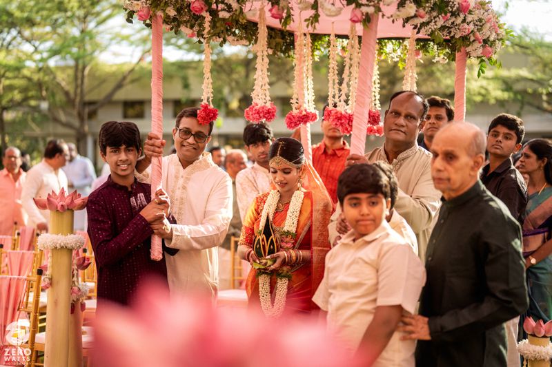 Indian wedding ceremony with bride and groom walking under a floral mandap surrounded by family members.