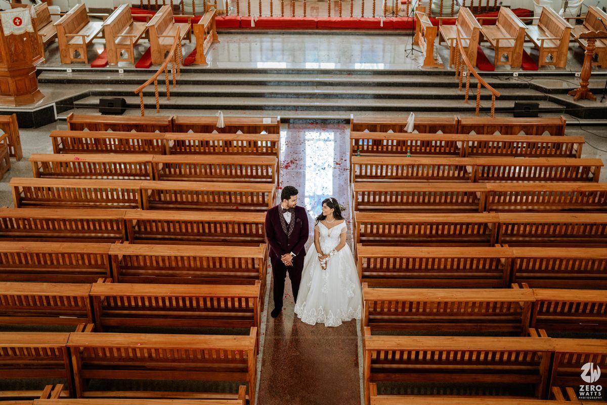 Aerial view of Indian wedding couple standing in aisle of elegant wooden church with pew rows.