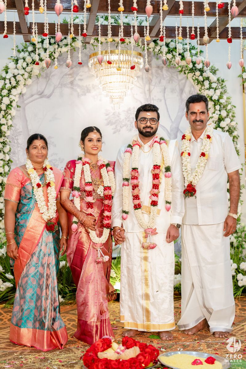 South Indian wedding couple in traditional attire with floral garlands pose with family under decorated floral mandap.