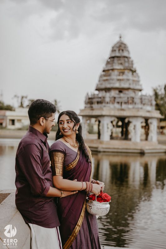 A romantic couple poses by a temple pond with traditional architecture and domed structures in the background.