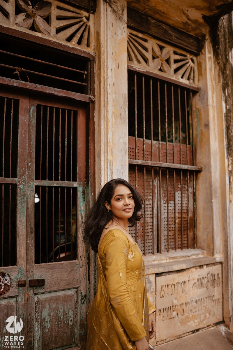 A woman in a yellow sari poses against a rustic doorway with vintage architectural details.