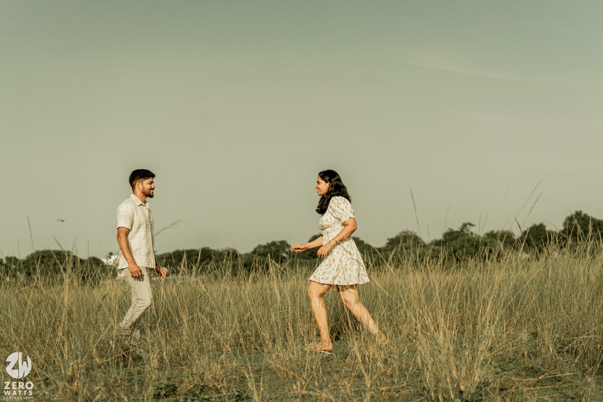 A couple playfully runs through a field of tall grass during an outdoor photoshoot.