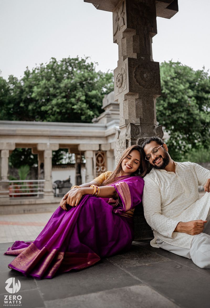 A couple in traditional Indian attire reclines on stone steps while sharing a romantic moment together.