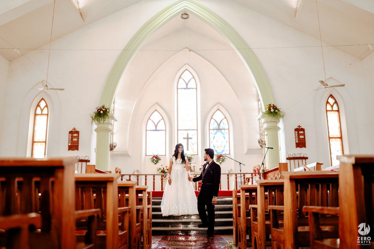 Bride and groom exchange vows at the altar of a beautiful white church with arched windows and wooden pews.