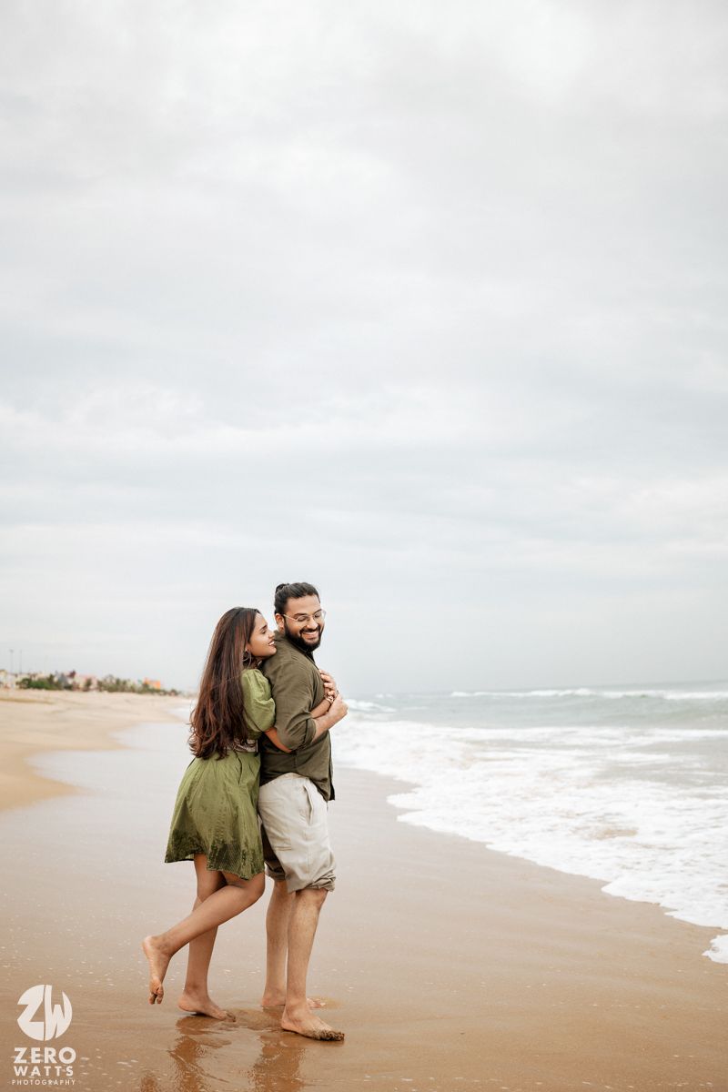Two people hold hands while walking along the shoreline of a peaceful beach.