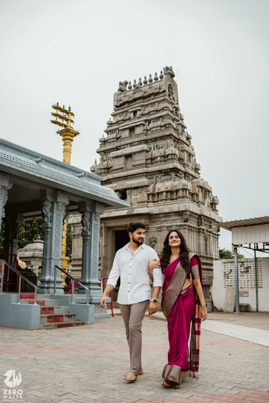 A couple walks outside a South Indian temple with traditional Dravidian architecture and gopuram tower.