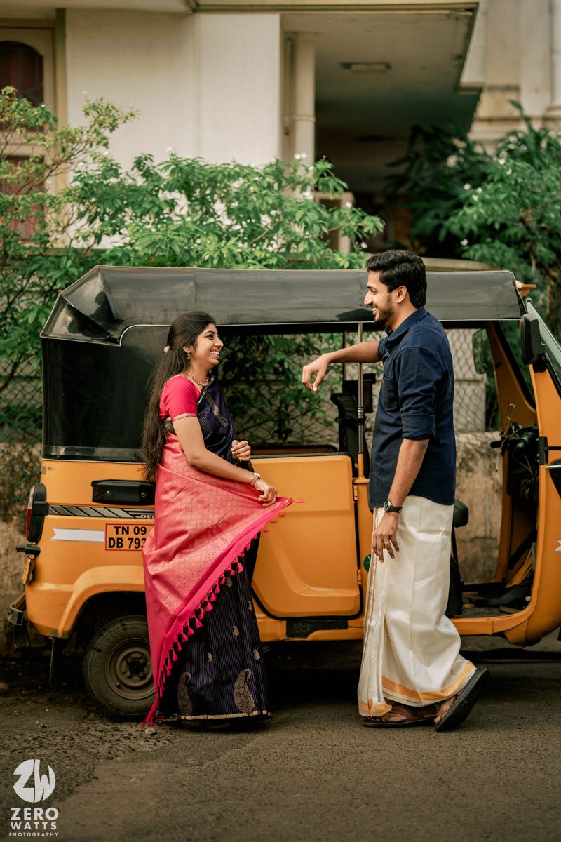 A couple poses playfully near a yellow auto rickshaw on a street.