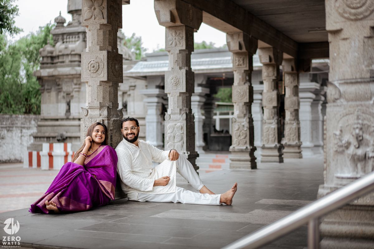 Couple in traditional Indian attire pose for wedding photos under ornate stone pillars and archways.