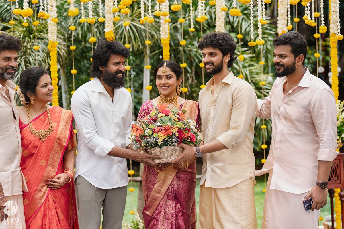 Wedding celebration with guests in traditional Indian clothing under yellow floral decorations outdoors.