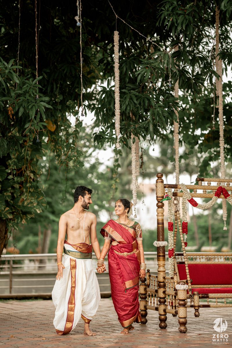 Traditional South Indian wedding ceremony setup with wooden pillars and red floral decorations in an outdoor setting.