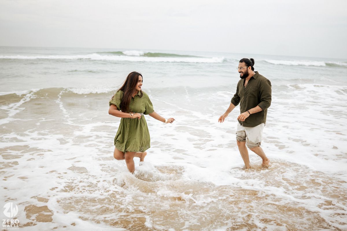 A couple plays and splashes together in the ocean waves on a cloudy beach day.