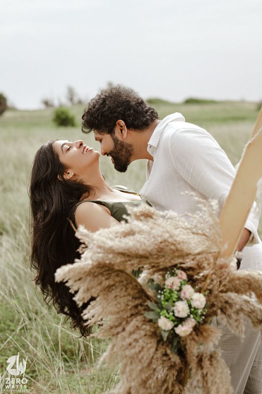 Romantic couple embraces in a sun-lit field of tall grass with dried pampas grass and floral bouquet.