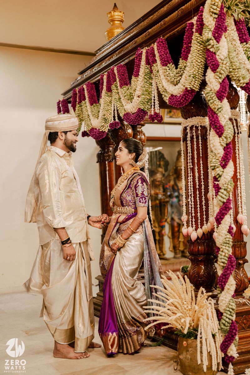 Traditional Indian wedding ceremony with couple under decorative mandap adorned with purple and white floral garlands.