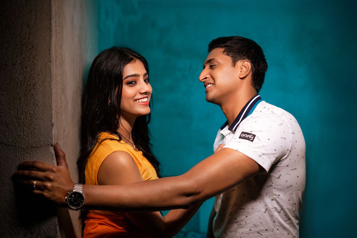 Couple sharing a playful moment against a turquoise wall background.