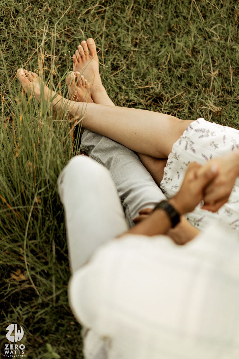 Bare feet resting on white fabric in a grassy outdoor setting during a romantic photoshoot.