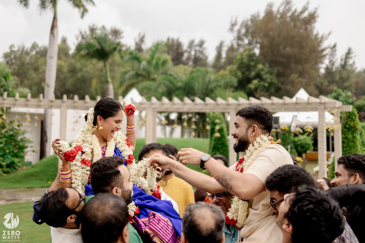 Wedding guests joyfully lift and celebrate during an outdoor ceremony with palm trees and greenery in the background.
