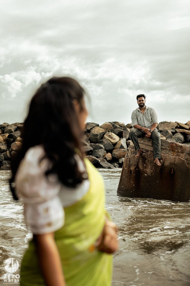 Romantic couple photoshoot on a rocky beach with dramatic cloudy sky.
