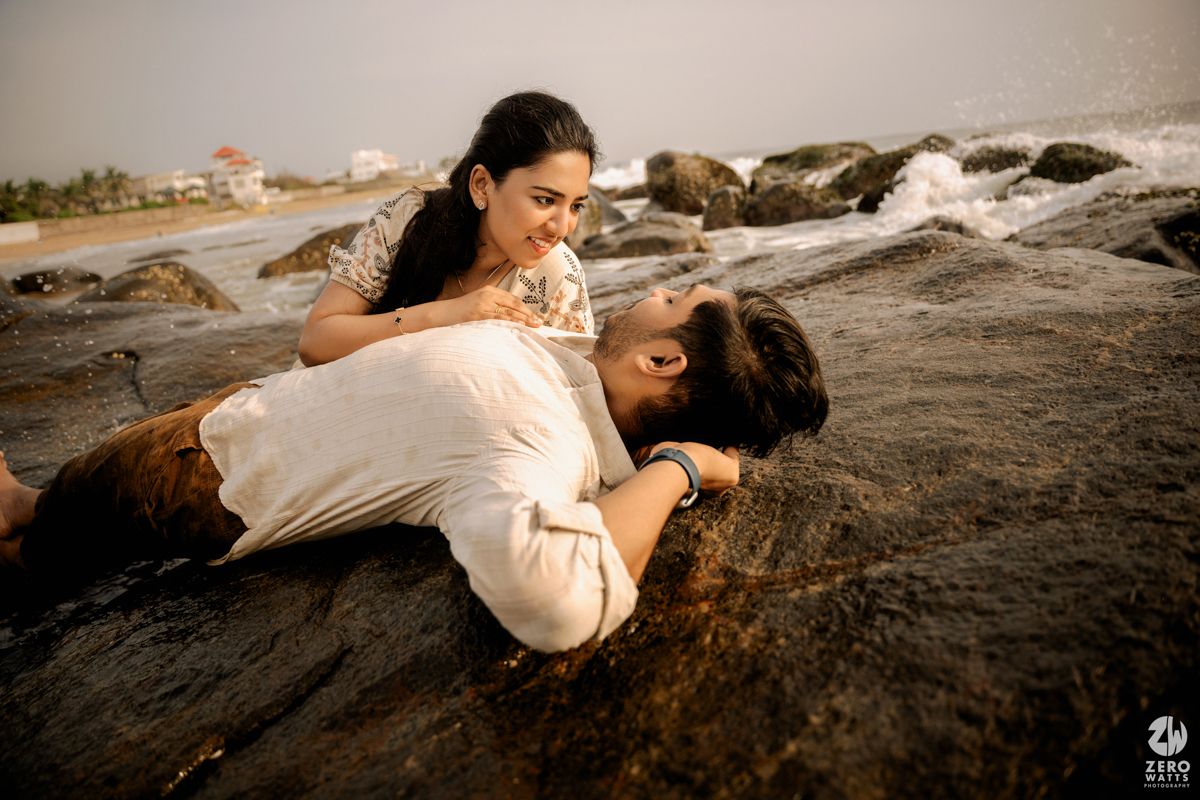 Couple embracing on coastal rocks during sunset maternity photography session.