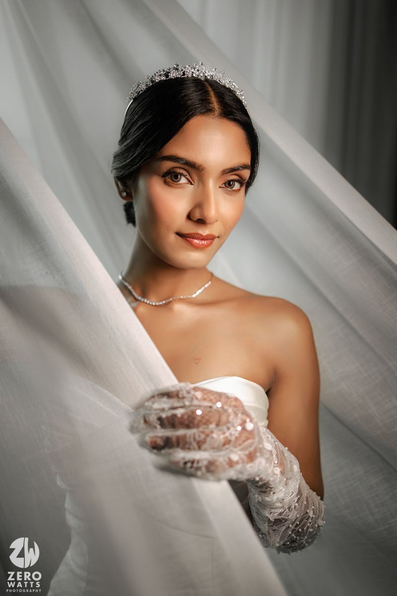 Beautiful bride wearing a crystal tiara, pearl necklace, and lace gloves in a white strapless wedding dress.