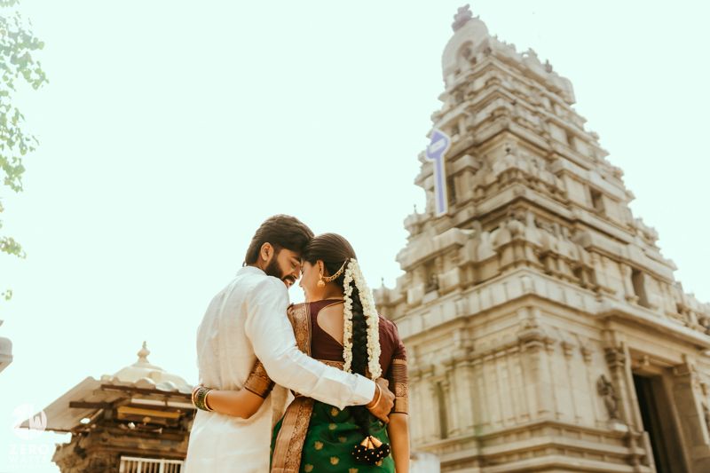 Couple embracing in traditional Indian attire before ornate temple tower during wedding ceremony.