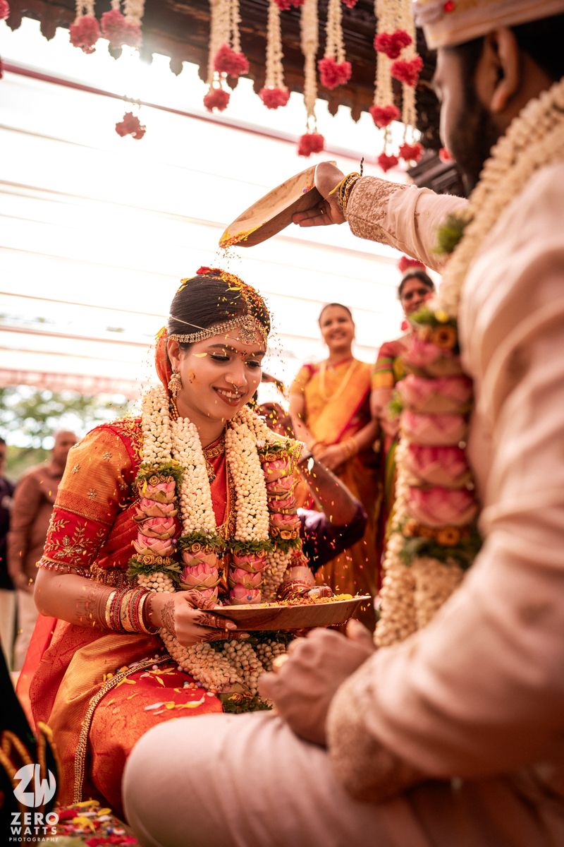 Bride smiles as sacred rice is poured over her head during a vibrant South Indian Hindu wedding ceremony.