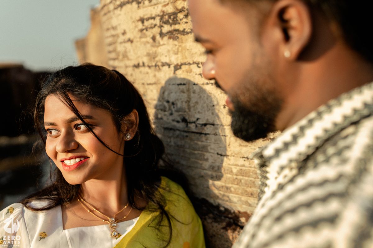 A couple shares a romantic moment at sunset against a brick wall, with warm sunlight creating atmospheric shadows.