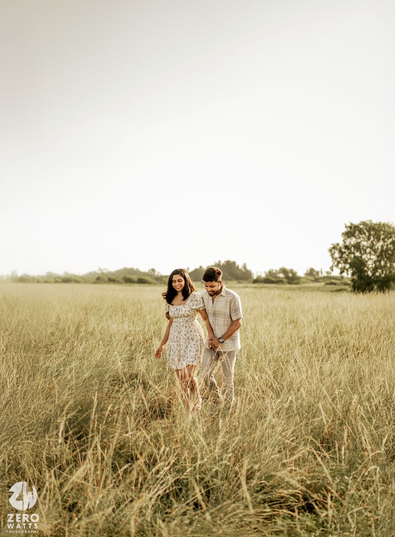 Romantic couple walking hand in hand through a serene golden wheat field at sunset.
