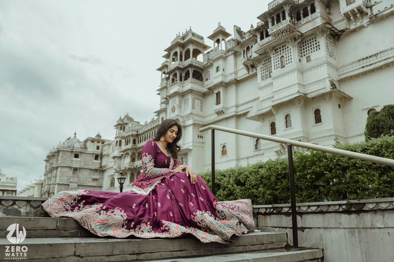 A person in a flowing magenta dress poses elegantly in front of the white City Palace in Udaipur, India.