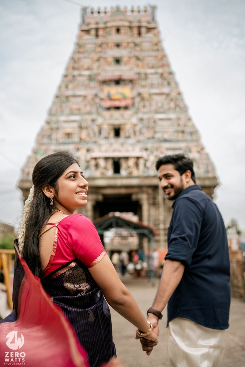 A couple poses for romantic photos in front of a traditional South Indian temple with ornate architecture.