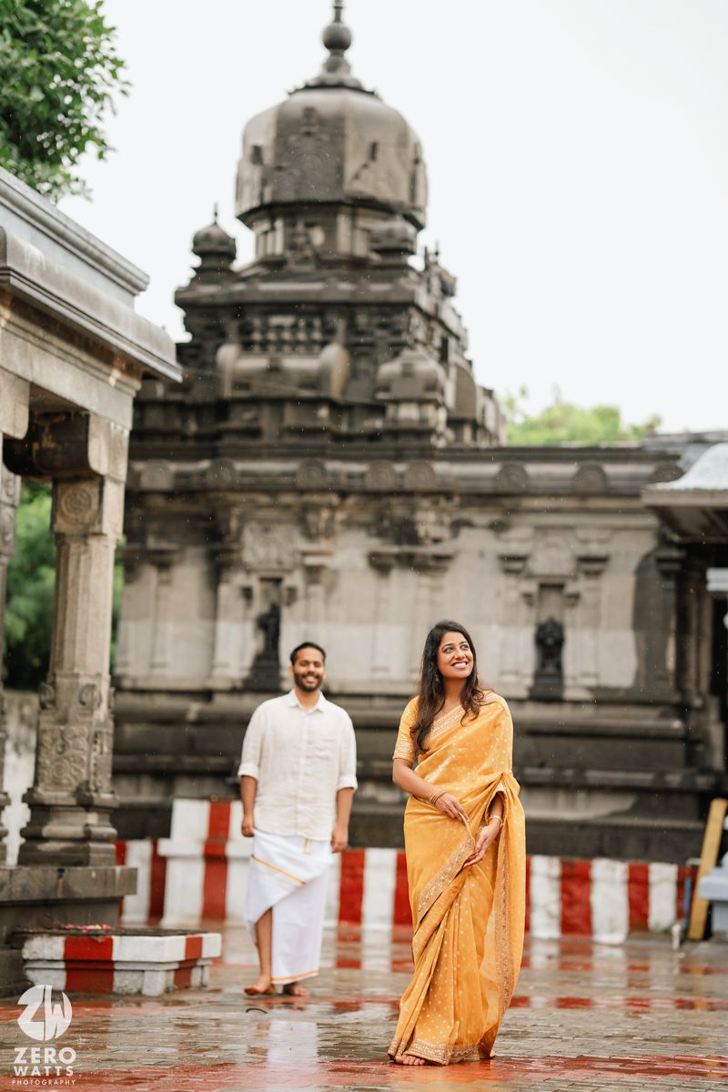 Traditional Indian engagement photoshoot at a historic temple with ornate architecture and stone columns in the rain.